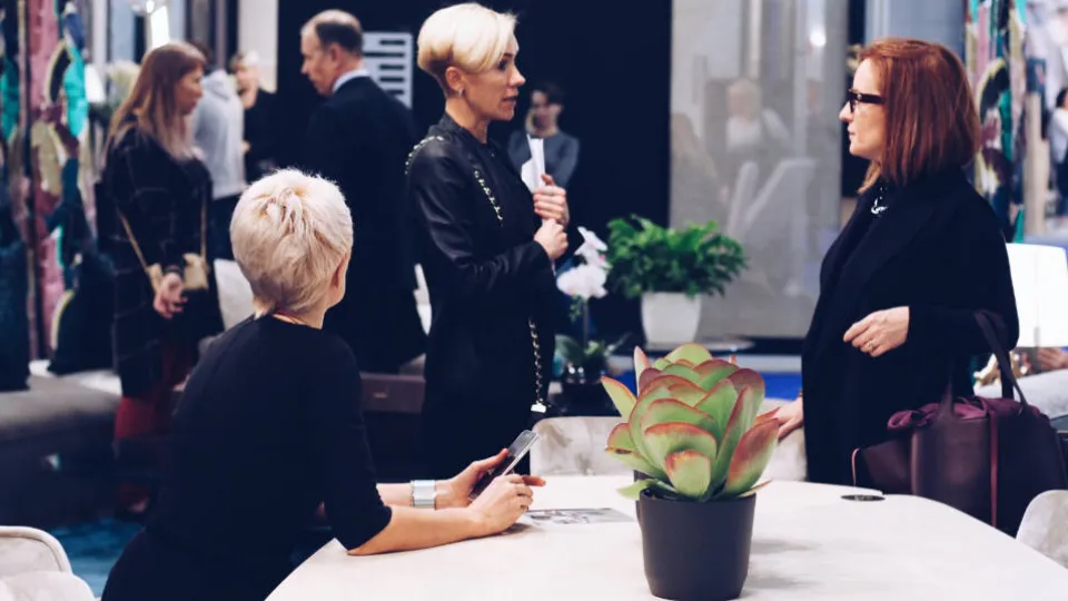 PIAAC Field Test successfully conducted Three women engaging in conversation at a fashion event with a potted plant in the foreground.