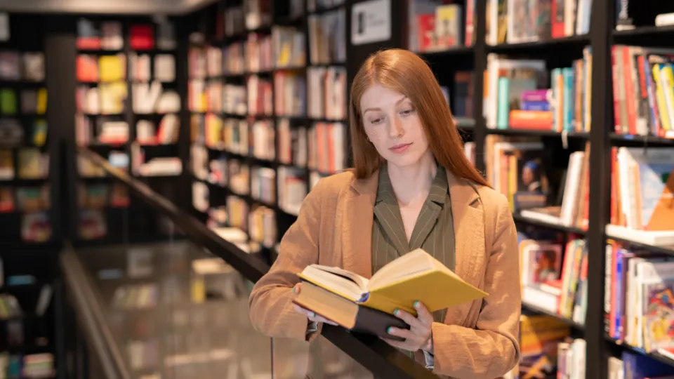 Livslångt lärande för framtidens arbetsmarknad. En ung kvinne leser en bok i en bokhandel med mange bøker i bakgrunnen.