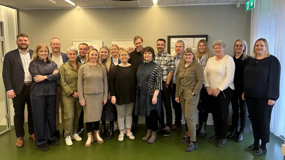 En gruppe mennesker som står sammen i et konferanserom, smilende for et gruppebilde.