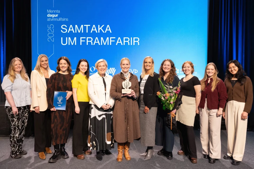 En gruppe kvinner står på en scene under "Mennta dagur atvinnulífsins 2025", med en pris og et diplom. En av dem holder en blomsterbukett. Bakgrunnen viser en blå skjerm med teksten "SAMTAKA UM FRAMFARIR".