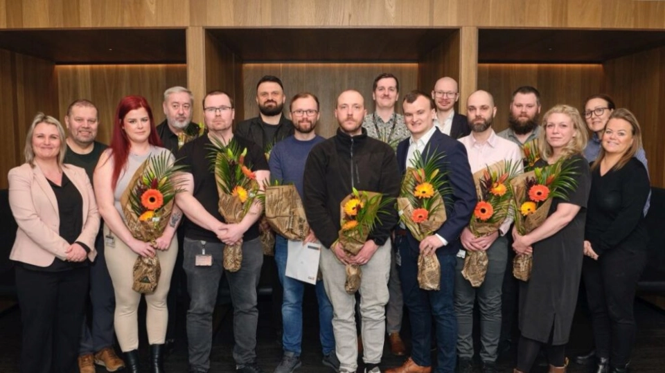 Mottok 14 sikkerhetsvakter hos Securitas fagbrev fra næringslivet En gruppe mennesker poserer for et bilde i en moderne innendørs setting, flere holder blomsterbuketter og ser fornøyde ut.
