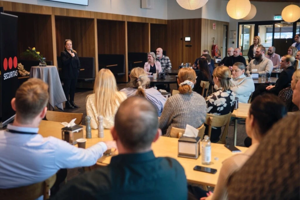 En kvinne holder en presentasjon for en gruppe mennesker i et konferanserom med Securitas-logoen synlig i bakgrunnen.