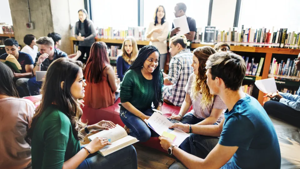 Ny rapport lyfter fram studieförbundens viktiga roll vid beredskap Studenter som sitter i grupp och studerar tillsammans i ett bibliotek, omgivna av böcker och naturligt ljus.