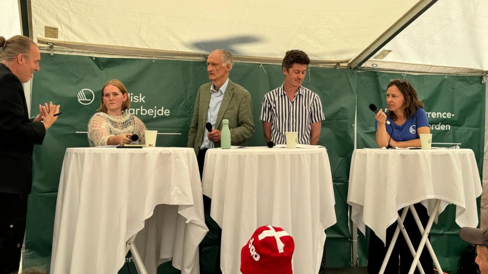 Panel discussion with five people under a tent, featuring microphones and drinks on standing tables, with a green backdrop labeled "Nordisk samarbejde."