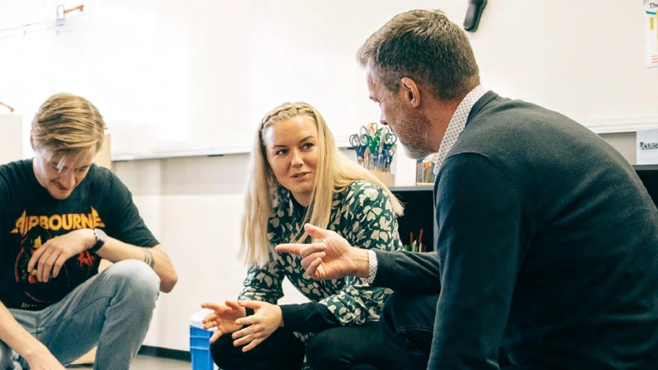 Professions- og erhvervs rettede videregående uddannelser til fremtiden Underviser i dialog med to voksne studerende i et klasseværelse, med tekst om højere kvalitet, fleksibilitet og livslang læring.