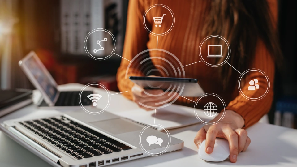 Så bekämpar Åland digitalt utanförskap Kvinna som använder surfplatta vid skrivbord med bärbar dator och digitala ikoner för nätverk, e-handel och kommunikation.