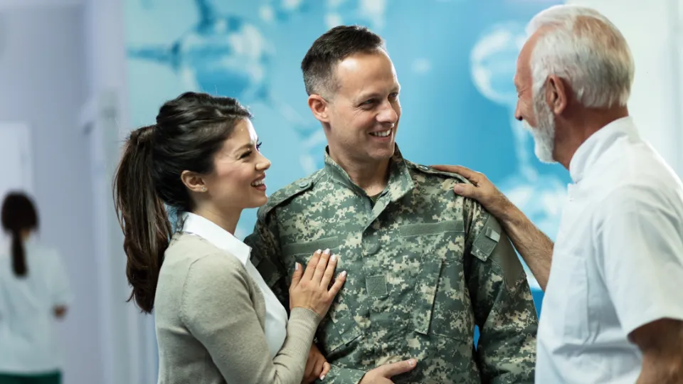 Smilende soldat i uniform sammen med familie, som snakker i et lyst sykehusmiljø.