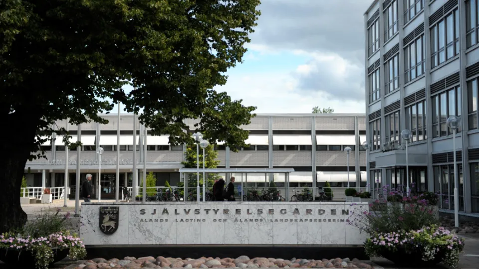 Exteriör av Självstyrelsegården, Ålands landskapsregerings byggnad, med stor stenskylt, blommor och kontorsbyggnader i bakgrunden.