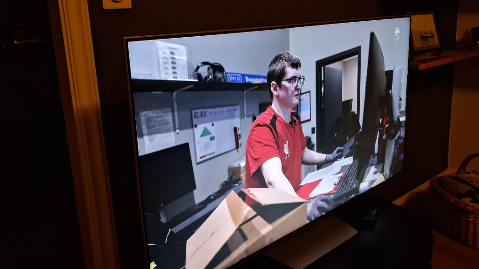 Davíð Smári Bjarnason i rød trøje arbejder ved en computer på en tv-skærm i et kontormiljø.